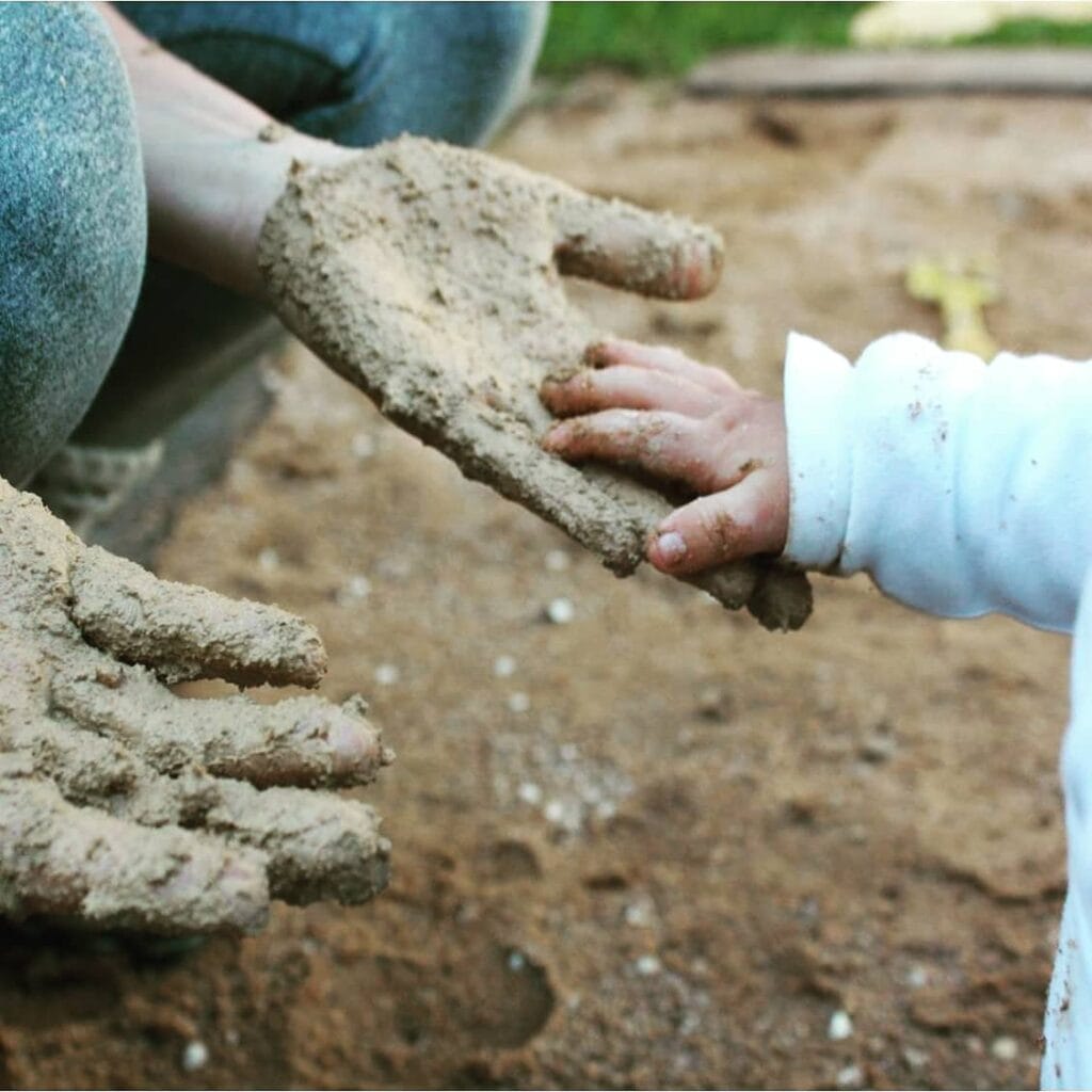 Mãos de adulto e criança cobertas de terra